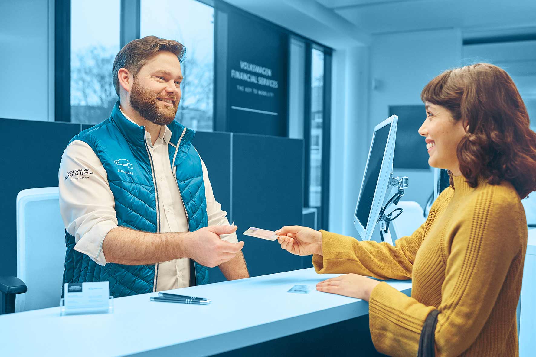 Stationsmitarbeiter bedient eine Kunden am Tresen in einer Station von VW FS | Rent-a-Car