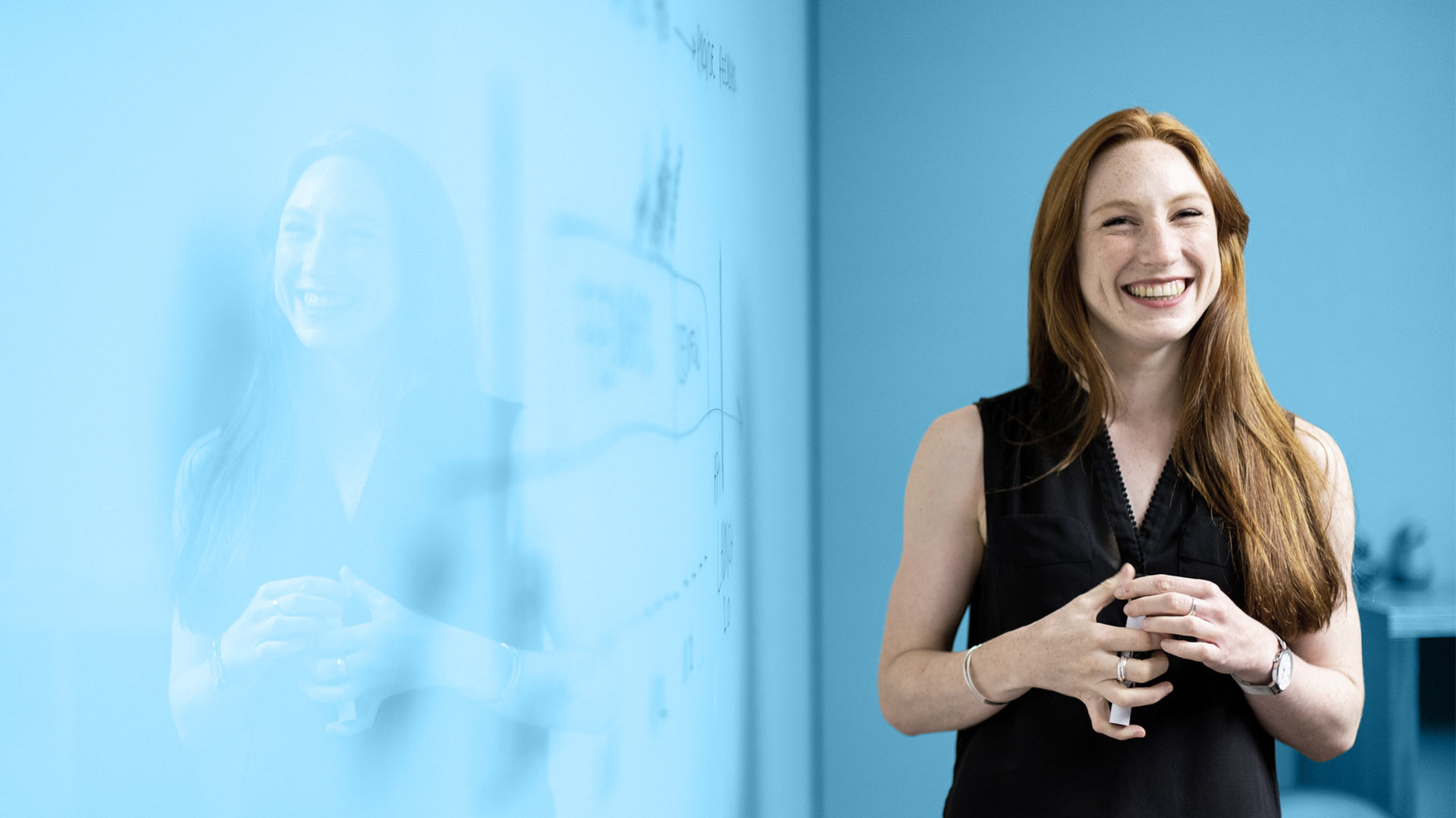 Junge, lächelnde Frau steht neben einem Whiteboard