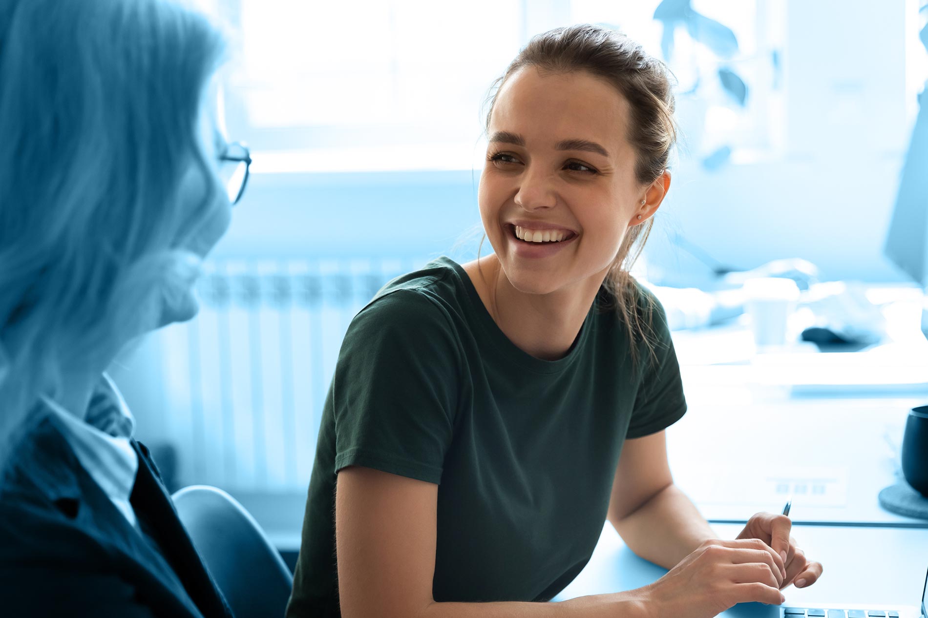 Junge, lächelnde Frau sitzt an einem Tisch und schaut zu einer Personalerin